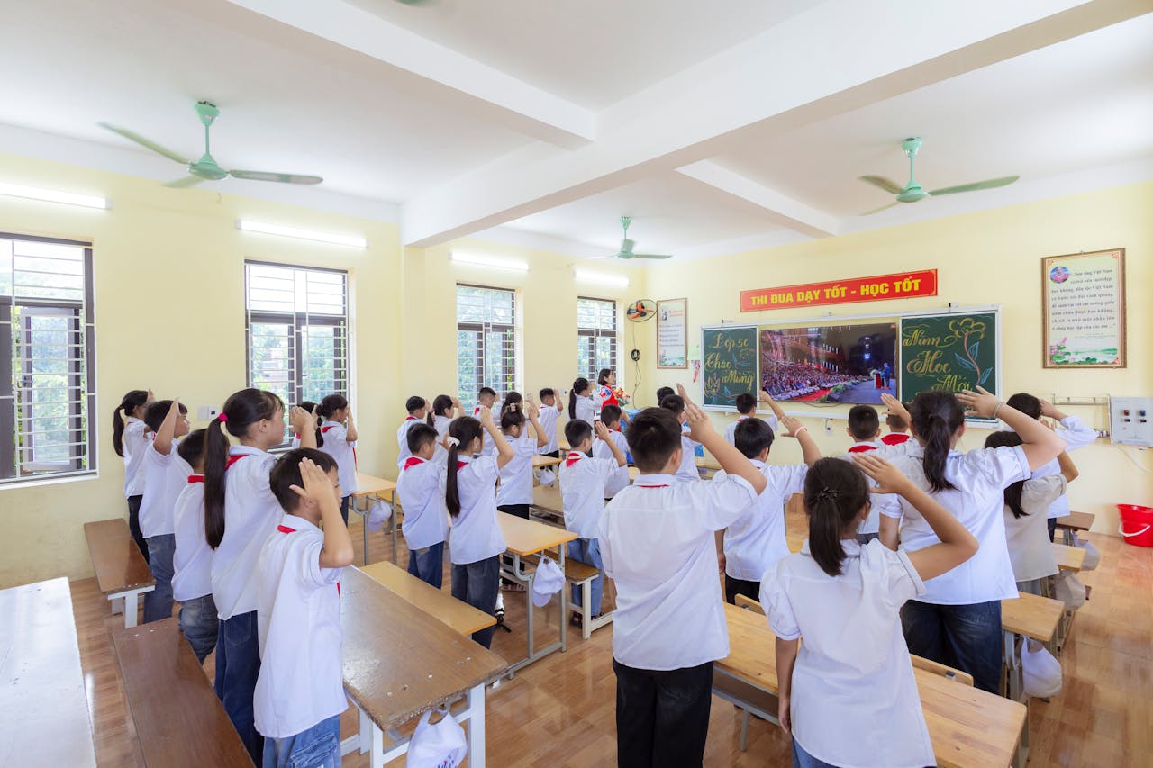 Students in uniforms saluting in a bright classroom during a school session.