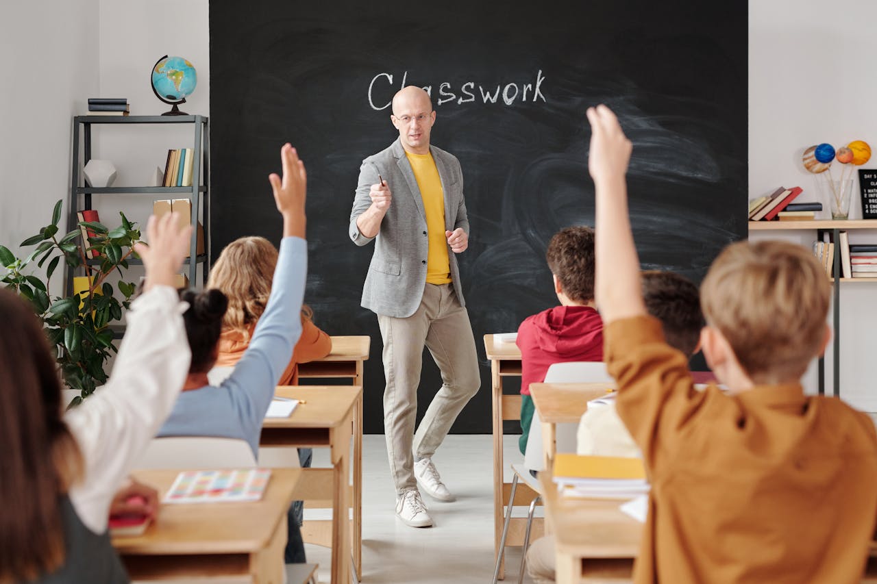 Teacher interacting with students raising hands in a classroom setting.